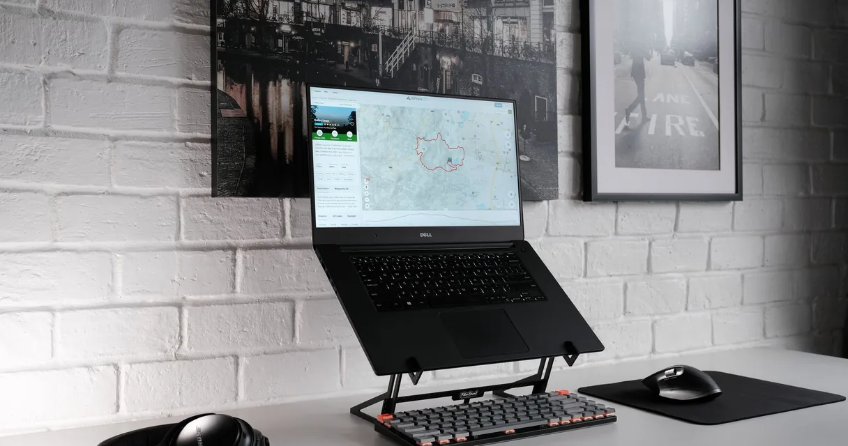 Notebook apoiado em suporte ergonômico sobre mesa, com fones de ouvido ao lado, ilustrando a dor no pescoço e a dor de cabeça