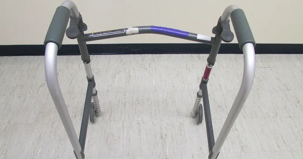 Andador de alumínio com apoios acolchoados em um piso claro, equipamento comum na fisioterapia domiciliar do paciente em recuperação