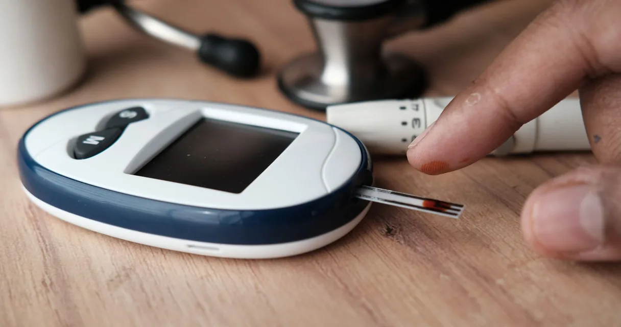 Hipoglicemia após bariátrica: glicosímetro sobre a mesa e dedo sendo furado para medir a glicose