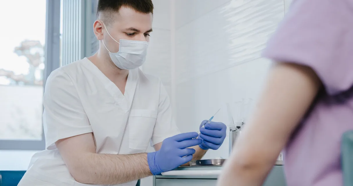 Médico de máscara preparando uma seringa em consultório