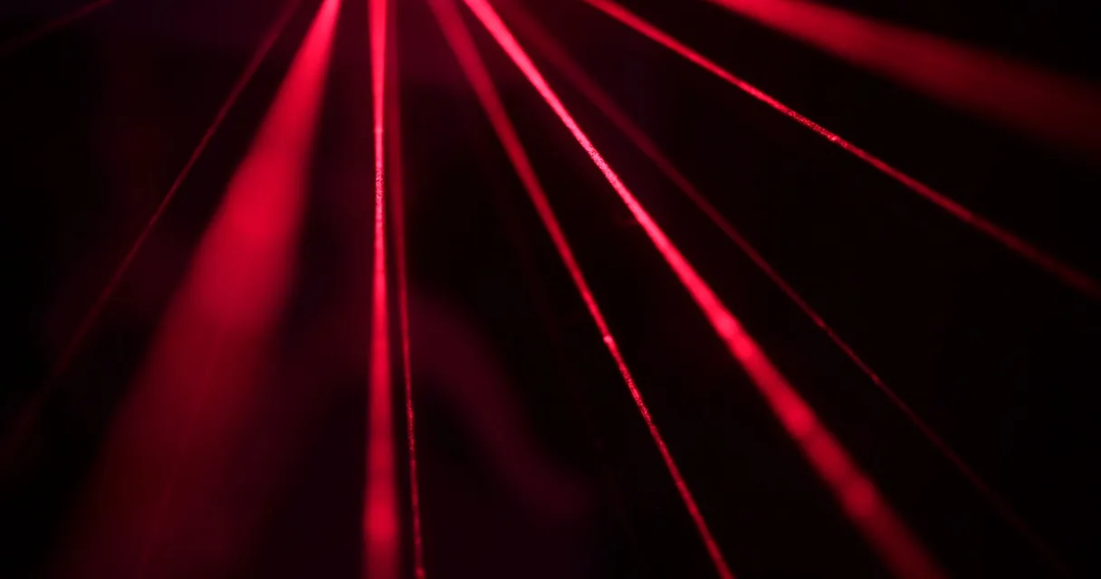 Feixes de luz laser vermelha sobre fundo escuro, ilustrando o laser fracionado para marcas na pele
