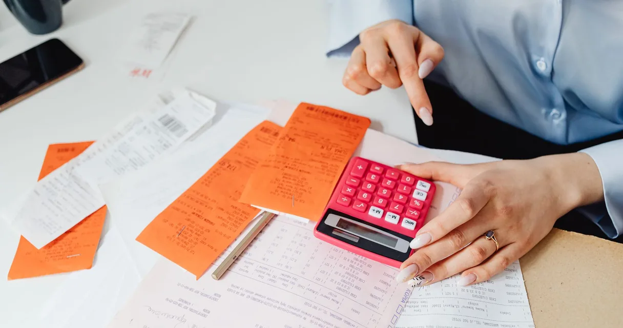 Mãos somando recibos em uma calculadora vermelha