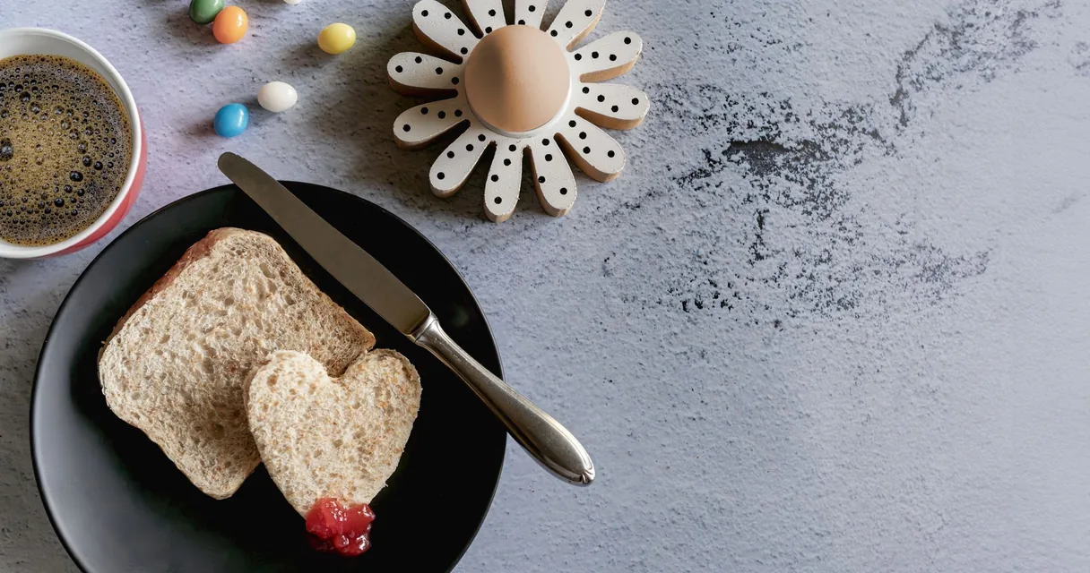 Mesa de café da manhã com xícara de café e pão com geleia, ilustrando a rigidez matinal nas mãos